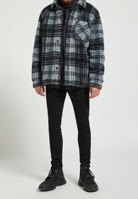 Rutigt jacka i svart och grått, tillverkad av mjukt tyg, med knappstängning och bröstficka. I kombination med svarta skinny jeans och sneakers.