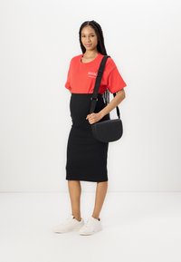 Rød kortermet t-skjorte med teksten "MAMA" kombinert med et svart midiskjørt med ribbestrikk, hvite sneakers og en svart crossover-veske med preget detaljer.