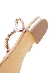Sandalia en rosa dorado con acabado metálico, correa en el tobillo ajustable, pequeñas joyas decorativas y suela plana de goma. Talla marcada 36.