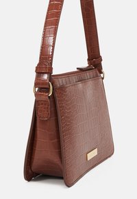 Sac à épaule en simili cuir marron avec une texture crocodile, doté d'une sangle réglable et d'un accent en métal doré.