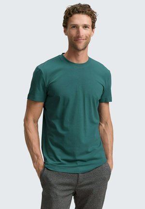 Turfkleurige crewneck t-shirt van zachte stof met korte mouwen. De aansluitende pasvorm accentueert de bovenlichaamsvorm; gedragen met grijze broeken.