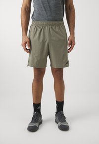 Khaki sportshorts med elastisk talje, sidelæg og et adidas-logo på venstre ben. Bæres med sorte sokker og grå sko.
