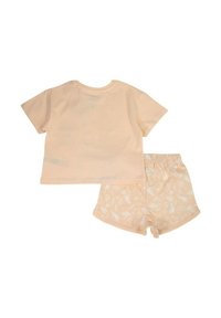 Ensemble t-shirt et short en coton pêche. Le t-shirt a des manches courtes ; le short présente des motifs floraux blancs. Tissu doux avec une coupe décontractée.