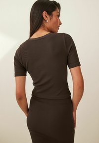 Ribbed brown top with short sleeves, round neckline, and a fitted silhouette. Textured material enhances visual interest, offering a subtle sheen.