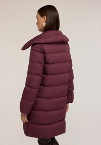 Burgundský péřový kabát s vysokým límcem, prošívaným designem, dlouhými rukávy a volným střihem. Hladký povrch a délka po kolena.