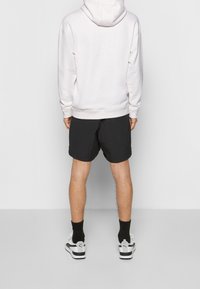 Bílý tečkovaný mikinový svetr, černé šortky, černé ponožky a bílé tenisky s černými akcenty. Mikina má šňůrku a klokání kapsu.