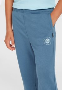 Blå bomullssweatpants med avslappnad passform, med sidofickor och en spiral-logotyp som accent vid fickan. Mjuk textur, elastisk midja.