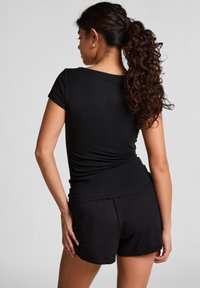 Haut noir ajusté à manches courtes associé à un short noir assorti. Tissu lisse et extensible avec un design simple et sans motifs ni quincaillerie visibles.