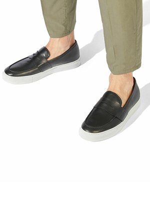 Czarne skórzane buty wsuwane z białą gumową podeszwą, charakteryzujące się smukłym kształtem, lekko podniesioną częścią palców oraz dekoracyjnym paskiem.