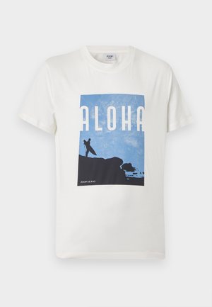 Fehér, rövid ujjú póló kék grafikával, amelyen egy szörfös látható, amint egy deszkát tart a sziklán, alatta az "ALOHA" felirat és a "JOOP! JEANS" logó.