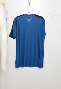 Camiseta atlética azul con paneles de malla negra en los hombros, mangas cortas, escote redondo y una tela texturizada. Etiqueta visible en el lado izquierdo.