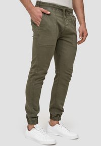 Olivgrüne Jogginghosen mit elastischem Bund, verstellbarem Kordelzug, Seitentaschen und eingesetzten Bündchen an den Knöcheln, hergestellt aus einer strukturierten Baumwollmischung.