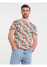 Květinové tričko s oranžovými a bílými květy hibiscus a zelenými listy na krémovém pozadí. Krátké rukávy a kulatý výstřih.