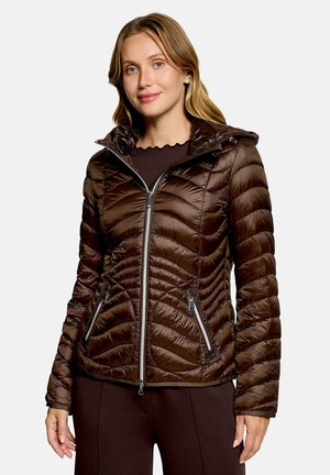 Woman wearing a shiny brown quilted jacket with a front zipper and zippered pockets, standing against a plain background.