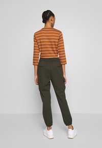 Randig brun topp med trekvartsärmar, som parats ihop med gröna cargobyxor med elastisk midja och uppvikta anklar. Vita sneakers.