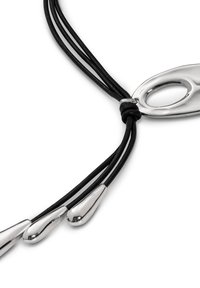 Collar de cordón de cuero negro que presenta un centro de metal plateado pulido con un corte ovalado, acentuado por tres extremos en forma de lágrima de plata.