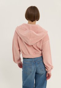 Sweat à capuche rose, côtelé et court, avec une grande capuche et des manches ballons, associé à un jean bleu taille haute. Éléments de design simples et modernes.