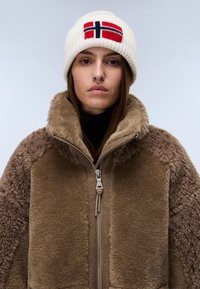 Chaqueta de forro polar marrón con tejido texturizado, cuello alto y detalles con cremallera. Gorro de punto blanco con diseño de la bandera noruega en rojo y azul.