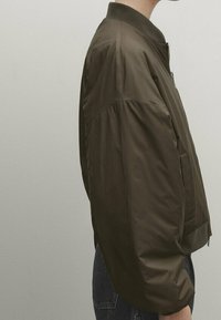 Braune Bomberjacke mit einem Reißverschluss vorne, elastischen Bündchen und einer glatten, glänzenden Textur. Sie verfügt über einen klassischen abgerundeten Kragen und seitliche Taschen.