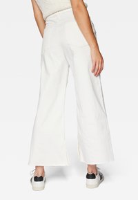 Valkoiset leveälahkeiset farkut rispaantuneilla helmilla, kahdella takataskulla ja korkealla vyötäröllä. Yhdistetty mustavalkoisiin lenkkareihin.