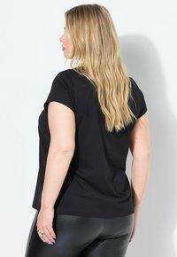 T-shirt nera a maniche corte con scollo rotondo, visualizzata dal retro, abbinata a leggings neri aderenti. Texture liscia.