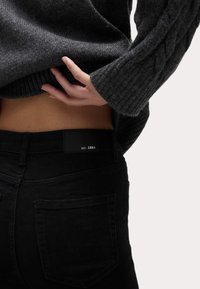 Černé džíny s hladkým povrchem a zadními kapsami. Šedý pletený svetr s copánkovým vzorem, částečně zakrývající pas.