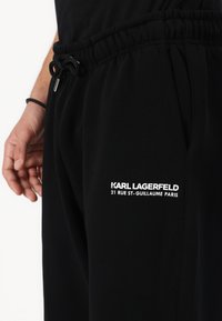 Melni sporta bikses ar elastīgu jostasvietu un auklu. Kreisajā kājā ir balts izšuvums ar logo tekstu. Gluda kokvilnas auduma materiāls.