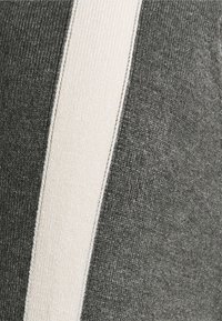 Szary dzianinowy materiał z szerokim kremowym paskiem, fakturowaną powierzchnią i różnymi odcieniami szarości, tworzący kontrast wzorów.