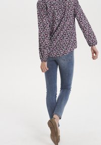 Blouse fleurie noire avec des fleurs roses et blanches, manches longues, coupe décontractée ; associée à un jean bleu ajusté et des ballerines marron.