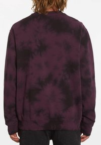 Lila sweatshirt med ett tie-dye-mönster i svart accent, långa ärmar, ribbade muddsydd, och rundad halsringning. Tillverkad av mjukt bomullsblandat material.