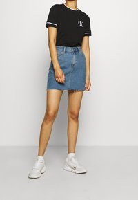 Svart bomullströja med vita detaljer, matchad med en ljusblå denimkjol med rå nederkant. Vita sneakers fulländar outfiten.