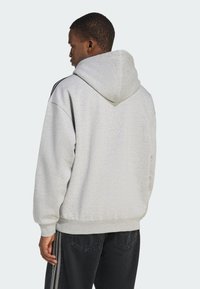 Sivá mikina s kapucňou vyrobená z textúrovaného materiálu, vybavená kapucňou so šnúrkou, rebrovanými manžetami a pruhmi po stranách na rukávoch.