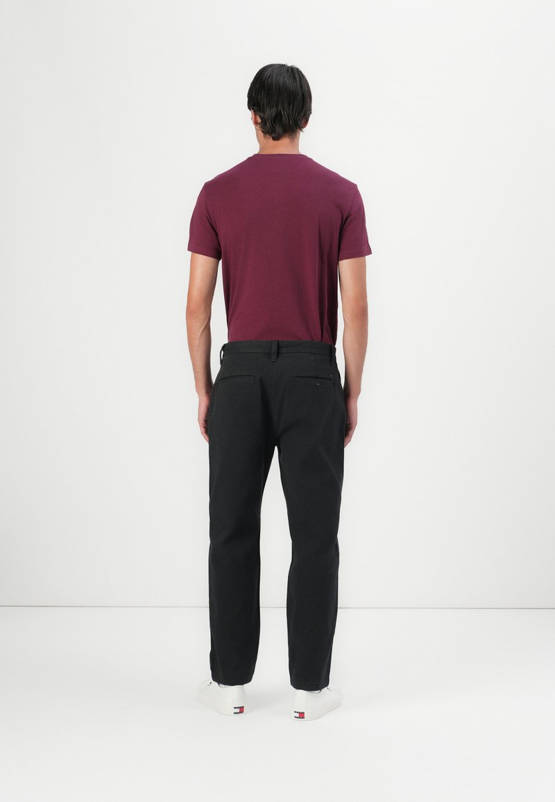 Bordeauxfarbens T-Shirt, schwarze Hose und weiße Sneakers. Einfaches Design, taillierte Form, glattes Material, minimale Details und zwei Taschen auf der Rückseite.