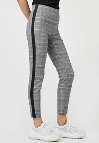 Gray plaid leggings with a black side stripe, featuring a fitted design and stretchy fabric, paired with white chunky sneakers.