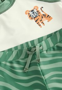 Pantaloni da bagno verdi con lacci in vita, caratterizzati da una stampa di tigre e un motivo a strisce ondulate verde chiaro e bianco sul tessuto.