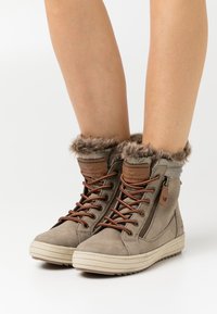 Bottes montantes en daim gris avec col en fausse fourrure, lacets marron et fermeture éclair sur le côté. Elles disposent d'une semelle plate et d'accents de marque sur la languette.