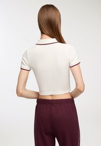 Polo bianco corto con bordino bordeaux, abbinato a pantaloni della tuta bordeaux con vita elasticizzata e strisce laterali. Texture liscia.