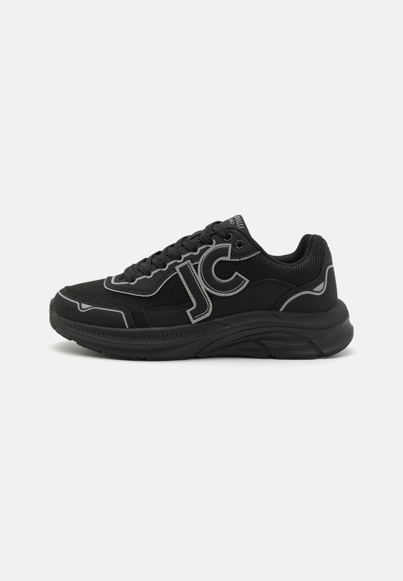 Zapatillas deportivas negras con materiales de malla y cuero, que presentan un atrevido logo "JC", costuras grises contrastantes y una suela gruesa texturizada.