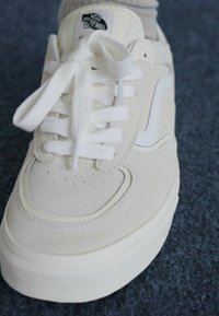 Vit lädersneaker med platta skosnören, rund tå och perforerade detaljer. Har en sidologga och en texturerad gummisula.