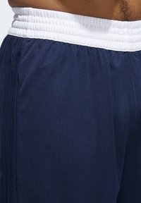 Marineblaue Sportshorts mit weißem elastischen Bund, aus atmungsaktivem Material gefertigt, mit glatter Textur und dezenten Perforationen.