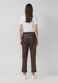 Bruine leren broek met een relaxte passing, voorzien van een elastische tailleband, zijzakken en een gladde textuur, gecombineerd met een witte t-shirt en platform schoenen.