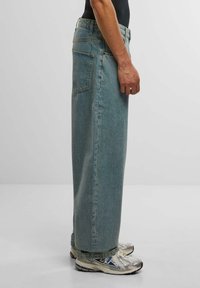 Lyseblå denimjeans med løs passform, sidelommer og rett snitt. Kombinert med sølvfargede joggesko.