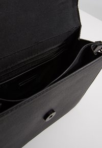 Wnętrze czarnej skórzanej torby z kieszenią na zamek i otwartą przegrodą. Gładka faktura z zapięciem na zatrzask. Minimalistyczny design.