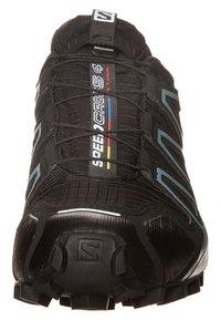 Zapatilla de correr negra con una parte superior texturizada y acentos reflectantes, que presenta un logotipo prominente, cordones y una suela resistente con tacos de tracción prominentes.