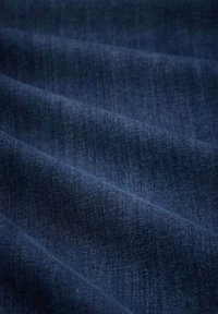 Material denim de culoare albastru închis, cu o textură fină, prezentând variații subtile de nuanță și un ușor luciu, evidențiind țesătura și căderea.