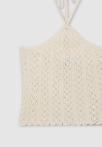 Top corto lavorato a maglia in crema, con orlo a scallop, motivo a rete e spalline regolabili. Tessuto morbido e materiale leggero.