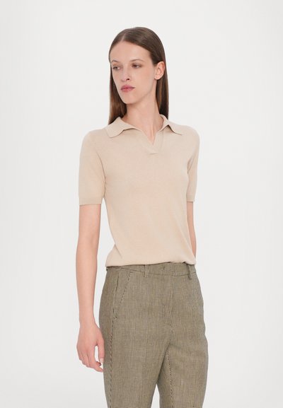 Polo a maglia beige con colletto corto e maniche corte, abbinato a pantaloni su misura con stampa a quadri.