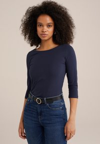 Marinblå långärmad topp med båtutskärning, kombinerad med högmidjade denimjeans och ett svart bälte med en gyllene cirkulär spänne.