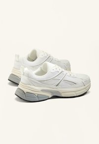 Sneakers bianche in rete con un design testurizzato, dotate di una suola in gomma grigia e sottili accenti tonali. Lacci e cuciture visibili.