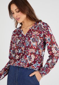 Blusa a maniche lunghe in tessuto borgogna, con un motivo floreale nei toni del blu, arancione e bianco. Scollo a v con incisione e vestibilità rilassata.